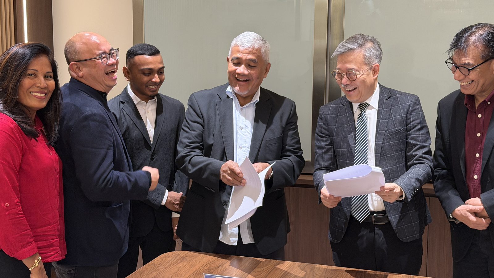 Datuk Eric Chong and Dato' Dr. Mohd Majid Konting exchanging the signed documents alongside colleagues from both teams